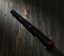 Load image into Gallery viewer, The Franklin-Christoph Model 02 Intrinsic Black &amp; Sweet Maroon pen lies diagonally on dark, rustic wood.