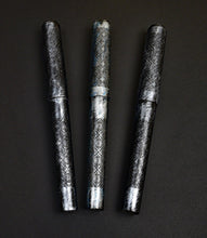 Load image into Gallery viewer, Three 03M Artisan Engraved Delrin pens by Franklin-Christoph with silver gothic motif are arranged on a dark background.