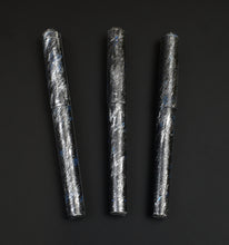 Load image into Gallery viewer, Three Franklin-Christoph 03M Artisan Engraved Delrin - Silver Gothic pens stand vertically on a black Delrin surface.