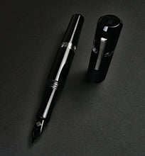 Load image into Gallery viewer, The Franklin-Christoph Model 19 Fountain Pen in Black &amp; Dark Room Emulsion rests uncapped on a dark, textured surface.