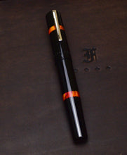 Load image into Gallery viewer, The Franklin-Christoph Model 19 Fountain Pen - Black Fire SE with orange accents rests on a dark surface.