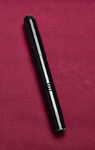 Load image into Gallery viewer, A closed Franklin-Christoph Model 46 Cor FP Black Cathedral pen lies diagonally on maroon fabric.