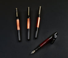 Load image into Gallery viewer, Four fountain pens on black background, including an uncapped Franklin-Christoph Model 55 Pentium Fountain Pen in Copper Rising.
