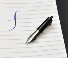 Load image into Gallery viewer, A Franklin-Christoph #6 Nib Unit rests on lined paper, with an elegant blue cursive “f” beside its gold tip.