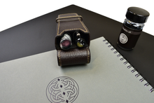 Load image into Gallery viewer, Franklin-Christoph Two Pen Case - Napa Brown holding two pens on a gray Celtic-knot notebook, beside a bottle of Graphite 4B ink.