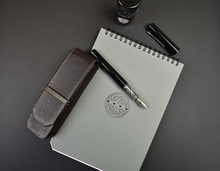Load image into Gallery viewer, Franklin-Christoph Two Pen Case - Napa Brown, gray notebook, fountain pen, ink bottle, and cap on a black surface.