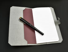 Load image into Gallery viewer, A Franklin-Christoph ETN - Black Napa w/ Suit Grey rests with a black pen on a black surface.