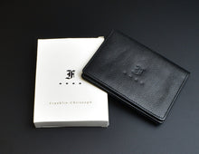 Load image into Gallery viewer, A black grained napa leather Franklin-Christoph Card Wallet with an embossed logo rests on a white Franklin-Christoph box, set against a black background.