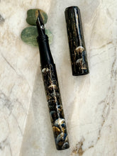 Load image into Gallery viewer, Franklin-Christoph 03M Foutain Pen called Moonlight On Umbrellas rests cap-off on marble with two green stones.