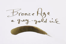 Load image into Gallery viewer, Handwritten text says Bronze Age, a grey-gold Franklin-Christoph Bottled Ink, above its matching shimmering swatch.