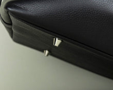 Load image into Gallery viewer, Close-up of a Franklin-Christoph Duffle Bag - Black Leather, showing two silver metal feet on the bottom corner.