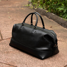 Load image into Gallery viewer, Franklin-Christoph Duffle Bag - Black Leather with handles on a stone path, ready for your next weekend getaway.
