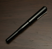 Load image into Gallery viewer, A Franklin-Christoph Model 02 Intrinsic Fountain Pen - Solid Black with silver clip rests on a dark wooden surface.