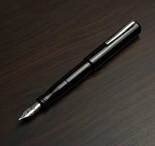 Load image into Gallery viewer, Franklin-Christoph Model 02 Intrinsic Fountain Pen - Solid Black with #6 nib and silver clip rests on dark wood.