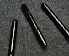 Load image into Gallery viewer, Three Franklin-Christoph Model 46 Cor FP Black Cathedral pens rest diagonally on textured gray fabric, evoking elegance.