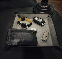 Load image into Gallery viewer, A Franklin-Christoph Valet Tray - Black Napa Suit Grey holds a watch, key, pouch &amp; knife on a black table.