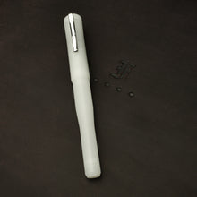 Load image into Gallery viewer, A frosted white Franklin-Christoph Model 02 Ghost pen with a silver clip lies near a stylized F on a dark surface.