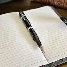 Load image into Gallery viewer, A Franklin-Christoph Model 19 Fountain Pen in Black &amp; Creme rests on an open, lined leather-bound notebook.