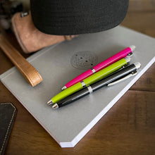 Load image into Gallery viewer, A Franklin-Christoph Model 28 Shortstock Ballpoint in Electric Lime sits on a gray notebook with two other pens.