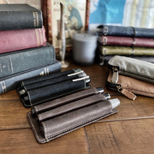 Load image into Gallery viewer, Franklin-Christoph Pen Case Inserts for 3 pens sit beside fountain pens, vintage books, and stationery on a wooden desk.