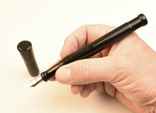Load image into Gallery viewer, A hand holds a Franklin-Christoph Model 50 Grandis Fountain Pen - Solid Black, uncapped against a light background.