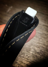 Load image into Gallery viewer, A close-up of the Franklin-Christoph Model 90 Artium Pencil - Black &amp; Creme’, featuring a black body and a white clicker, partially inserted into a black leather pen loop with yellow stitching. The background is a blurred brown surface.