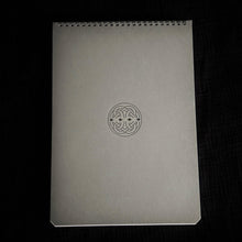 Load image into Gallery viewer, A Franklin-Christoph Greypads spiral sketchbook with a Celtic knot cover rests on a black surface.