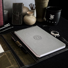 Load image into Gallery viewer, A Franklin-Christoph Greypads notebook sits in a leather folder, with a fountain pen, wristwatch, and desk accessories.