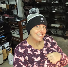 Load image into Gallery viewer, Smiling person in a bird-print shirt, wearing a Franklin-Christoph F-C Beanie, sits indoors near shelves and bins.