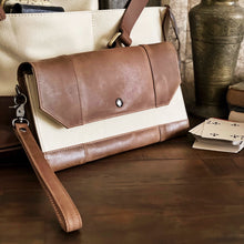 Load image into Gallery viewer, Franklin-Christoph Fortis Sling Bag in Creme’ and Brown on a wooden table with playing cards, books, and a vase.
