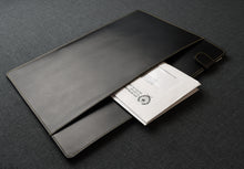Load image into Gallery viewer, A Franklin-Christoph Document Folder - Black Leather, partially open to reveal papers inside, rests on a dark gray fabric surface.