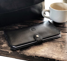 Load image into Gallery viewer, Black leather wallet on a wooden surface with a white mug in the background