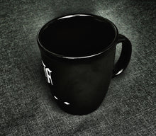 Load image into Gallery viewer, The Franklin-Christoph Coffee Mug 1 in matte black with a handle sits on a dark, textured fabric surface.