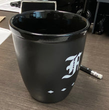 Load image into Gallery viewer, Franklin-Christoph Coffee Mug 1, matte black with white M and three diamonds, on desk near pencil and papers.