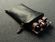 Load image into Gallery viewer, A Franklin-Christoph Glasses / Pen Case in black napa leather rests on a gray surface, partially open to reveal three fountain pens.