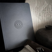 Load image into Gallery viewer, A Franklin-Christoph Greybooks A5 notebook with a Celtic knot cover is beside old papers, ink jar, and pen paper.