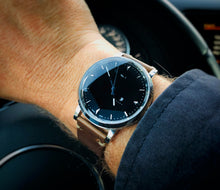 Load image into Gallery viewer, A person wearing a Franklin-Christoph IWO Timepiece grips a steering wheel inside their car.