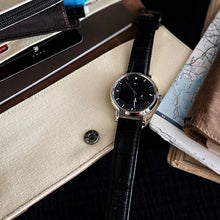 Load image into Gallery viewer, The Franklin-Christoph IWO Timepiece lies on a folder next to a map, pen, notebook, and its black leather strap gleams.