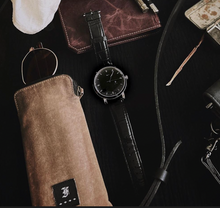 Load image into Gallery viewer, Franklin-Christoph IWO Timepiece in black leather, sunglasses with brown case, and leather goods on dark tabletop.