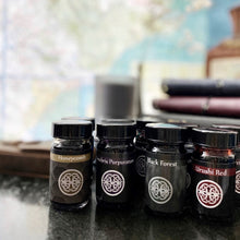 Load image into Gallery viewer, Franklin-Christoph Bottled Ink in Honeycomb, Black Forest, and Red lined up neatly on a desk.