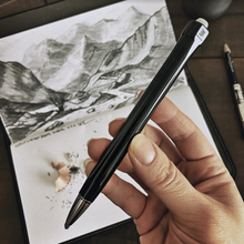 Load image into Gallery viewer, Hand holding a Franklin-Christoph Model 90 Artium Pencil - Black &amp; Creme’ near sketchbook and 3.15 lead shavings.