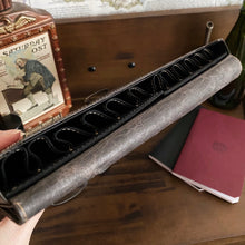 Load image into Gallery viewer, A hand holds the Franklin-Christoph New Penvelope 12 NWF near closed books and a vintage decorative tin.