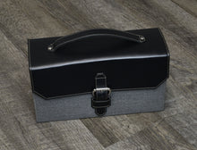 Load image into Gallery viewer, The Franklin-Christoph Christoph 48 Pen Case in black and gray with handle and buckle rests on a wooden floor.