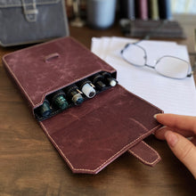 Load image into Gallery viewer, A hand opens a Franklin-Christoph New Penvelope 6 NWF with ink, glasses, and papers visible on the desk in back.