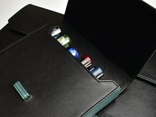 Load image into Gallery viewer, A partially open Franklin-Christoph Penvelope 12 Black Teal Leather case reveals colorful fountain pens inside.