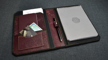 Load image into Gallery viewer, Franklin-Christoph Greypads leather portfolio holds notebook, pen, passport, cards &amp; docs on dark fabric surface.