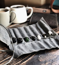 Load image into Gallery viewer, A Franklin-Christoph Seven Pen Roll filled with pens rests by a white teapot and mugs on a wooden table.