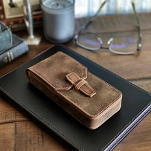 Load image into Gallery viewer, A Franklin-Christoph New Penvelope 3 Boot Brown Leather case sits on a black notebook, with glasses and a candle behind.