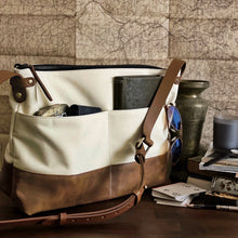 Load image into Gallery viewer, The Franklin-Christoph Fortis Sling Bag - Creme’ and Brown rests on a table with sunglasses, cards, and a wallet nearby.