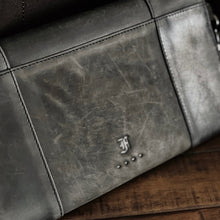 Load image into Gallery viewer, Close-up of Franklin-Christoph’s Fortis Clutch Envelope—Iron Brown &amp; Black—showing stitching and logo on wood.